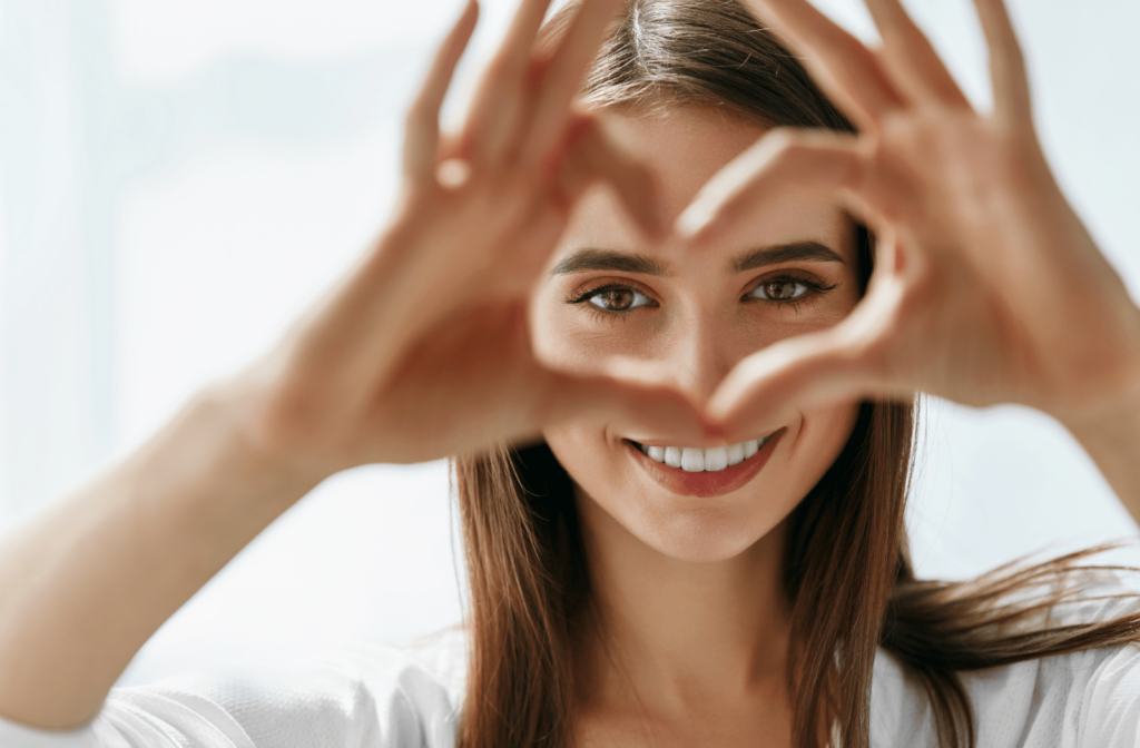 A young woman making a heart shape with her hands where her eyes are inside of the heart shape