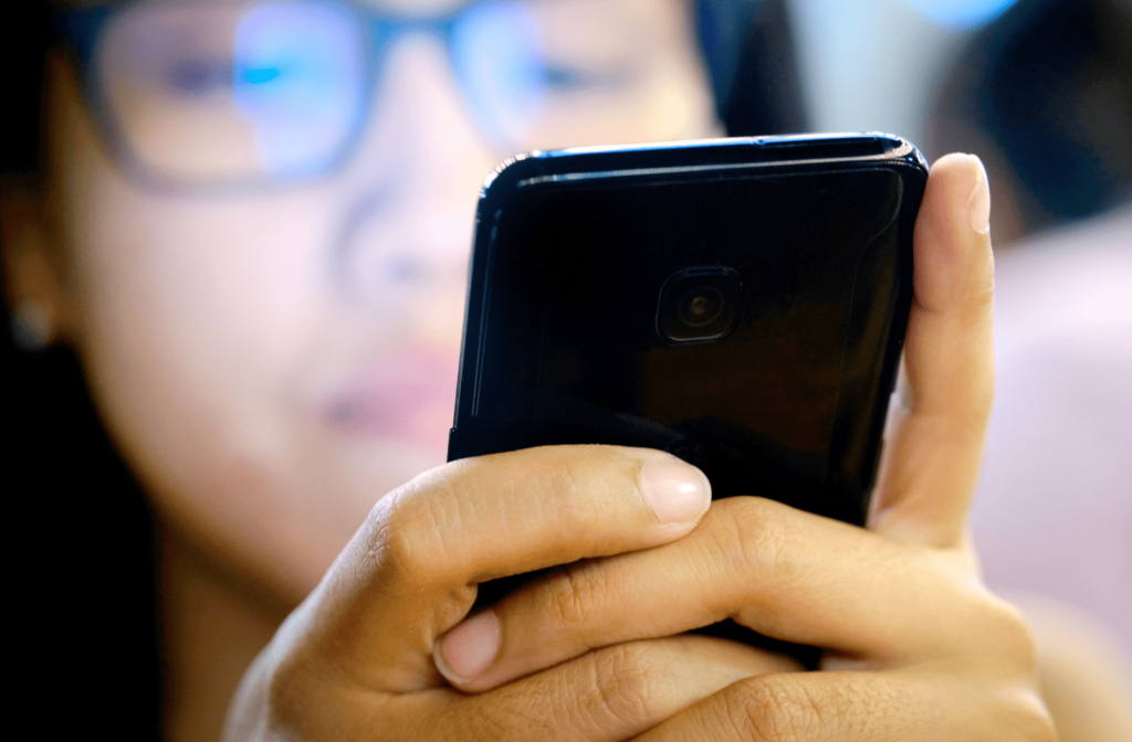 A woman wearing glasses and looking at her smartphone closely in her hands